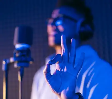 Image of the hand of a man in a studio recording booth showing the 'excellent' sign.