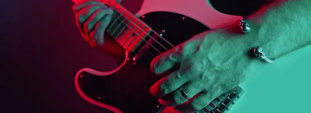 Close up of a white electric guitar body being played by someone with a golden ring and a silver bracelet