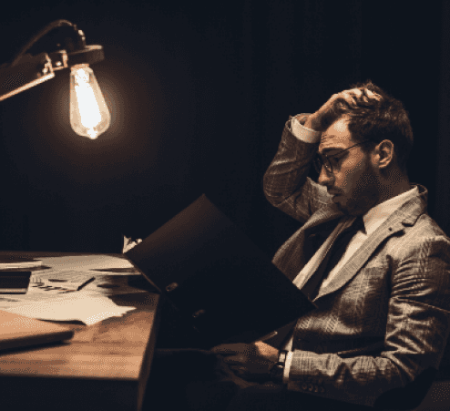 Man sitting behind a desk with a cosy light, scratching his hair reading a paper